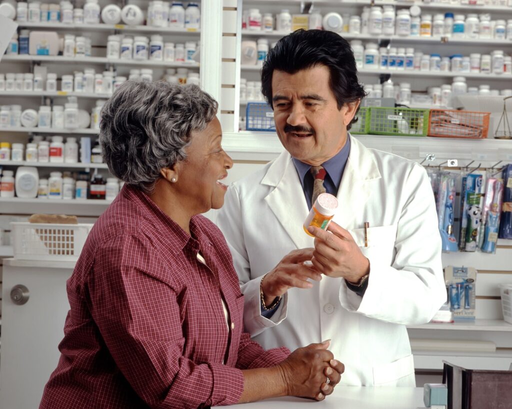 Woman Consults with Pharmacist. An older African-American woman talks to a Hispanic male pharmacist as he explains her prescription. Photographer Rhoda Baer